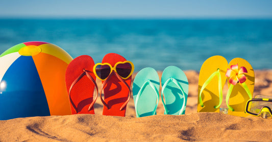 3 colorful flip flops and a beach ball in the sand on the beach. Photo by Sunny Studio/Shutterstock.com