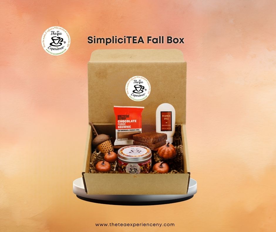 SimpliciTEA Fall Box gift set displayed in an open kraft cardboard box, featuring a chocolate bar, tea tin, candle, acorns, and small pumpkins, set against a warm orange gradient background.
